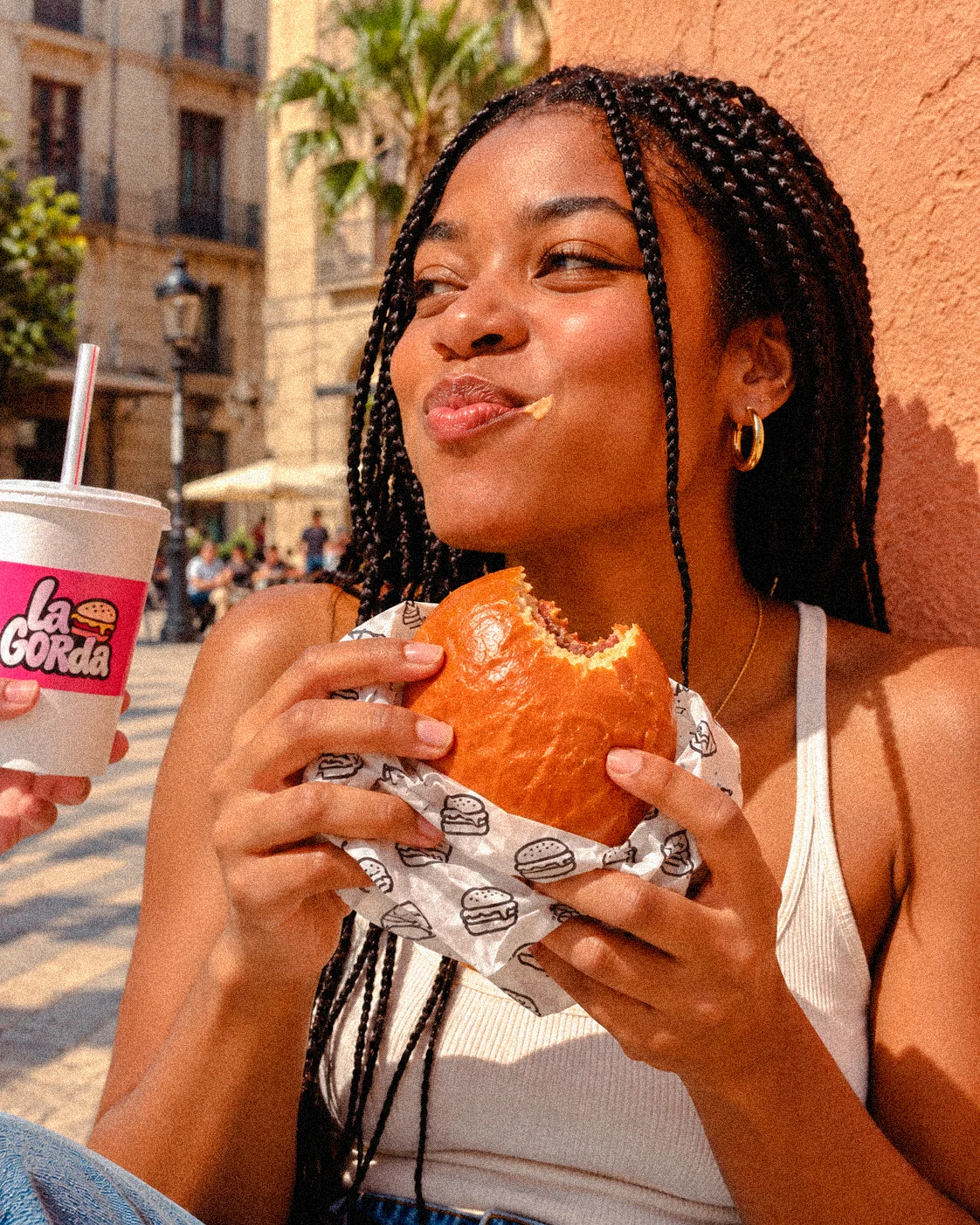 Una chica saborea una Rosa Picante junto a una plaza, con el vaso rosa de La Gorda